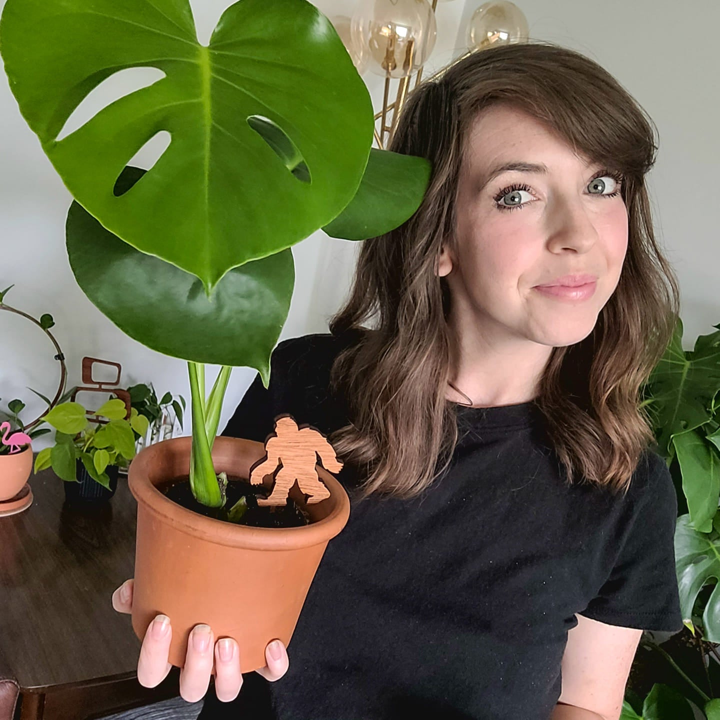 Jessy holding a small monstera plant in a clay pot with a bigfoot plant stake.