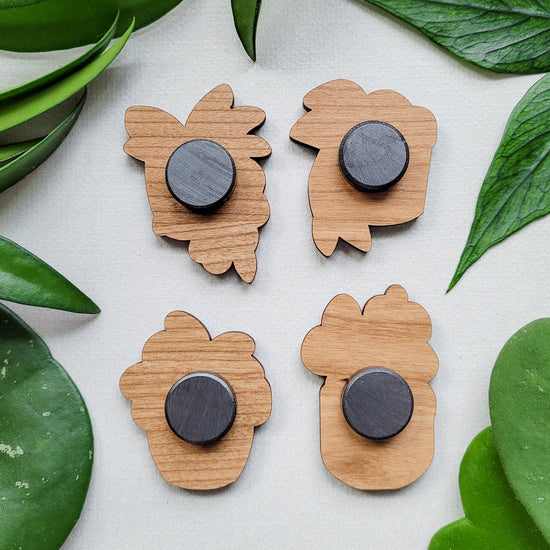 Backs of four handcrafted magnets featuring different hoya plant designs engraved in cherry wood.