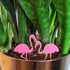Pair of pink flamingo plant stakes in a gold planter with a snake plant.