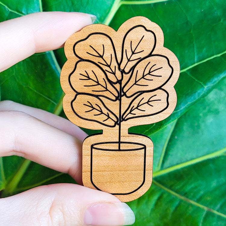 Handcrafted magnet featuring a fiddle leaf fig plant engraved in cherry wood held in hand for size perspective.