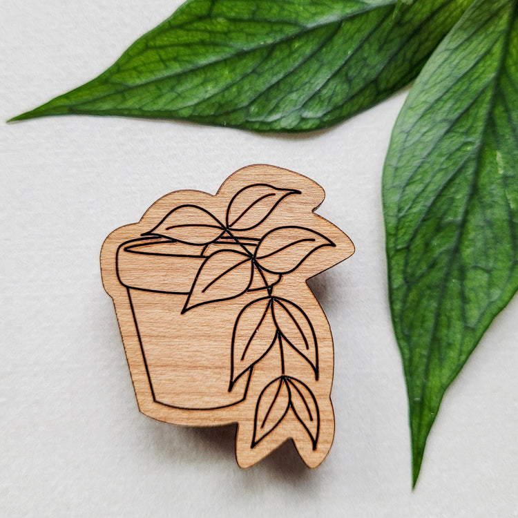 Handcrafted magnet featuring a hoya polyneura engraved in cherry wood against a white background and leaves from the plant..