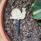 Single snail decorative plant stake laying on top of the soil in a clay pot containing a cactus.