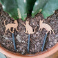 Set of three cat silhouette decorative plant stake laying on top of the soil in a clay pot containing a cactus.