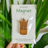 Handcrafted magnet featuring a snake plant engraved in cherry wood held against a plant in product packaging.