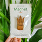 Handcrafted magnet featuring a snake plant engraved in cherry wood held against a plant in product packaging.