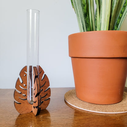 Wooden monstera leaf stand holding a clear test tube sitting on an end table with a snake plant in a clay pot.
